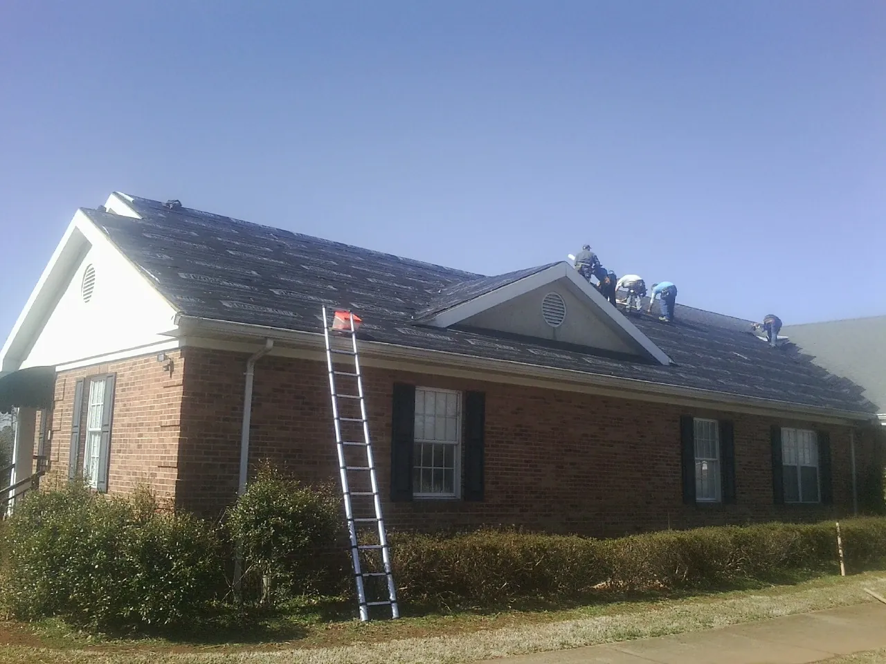 Crew tearing shingles off a brick ranch roof with a ladder set — Emergency Roof Repair work by our crew in Kaylor