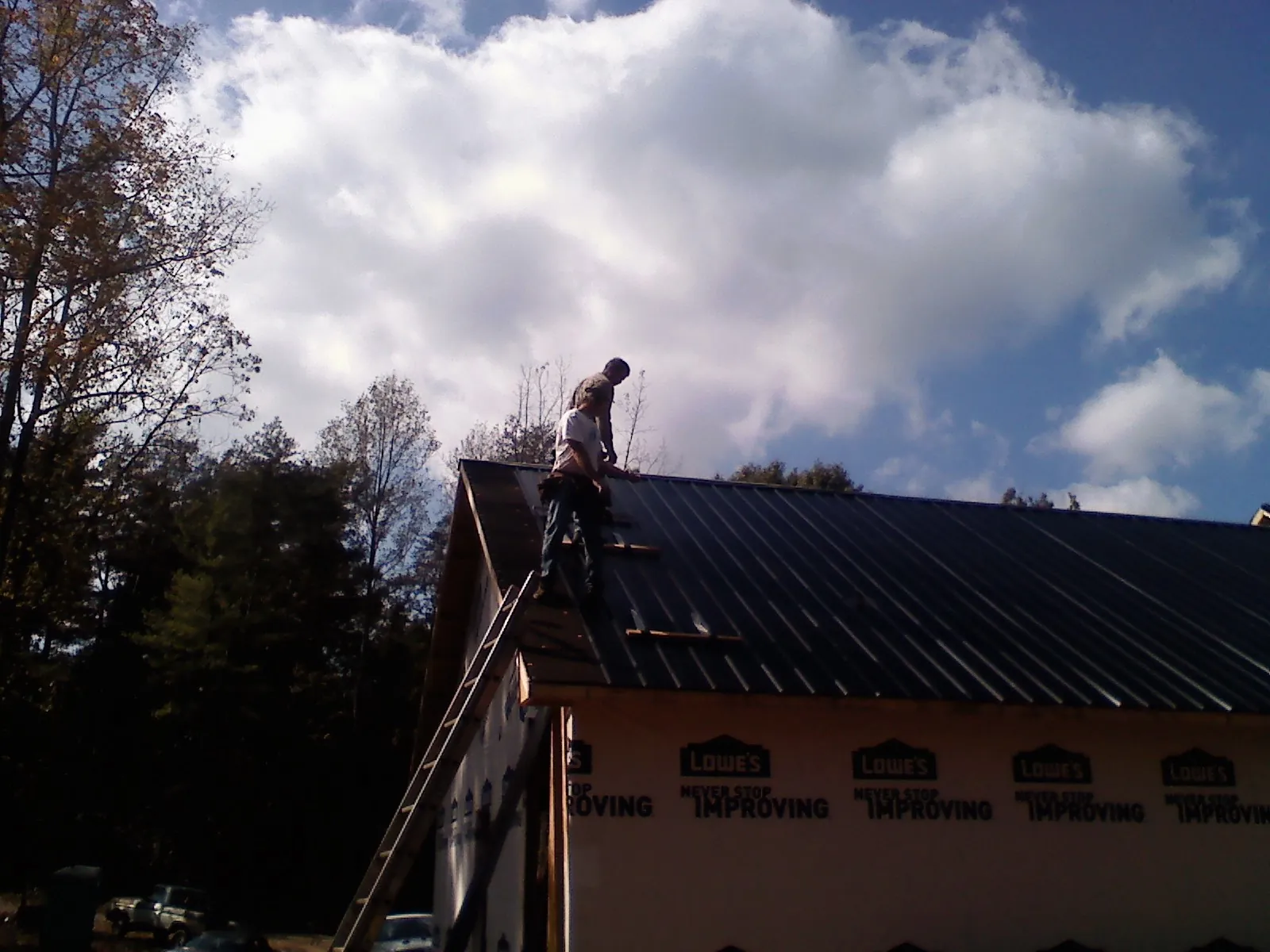 Roofer fastening dark metal panels high against a cloudy sky, from a Roof Inspection job in Kaylor